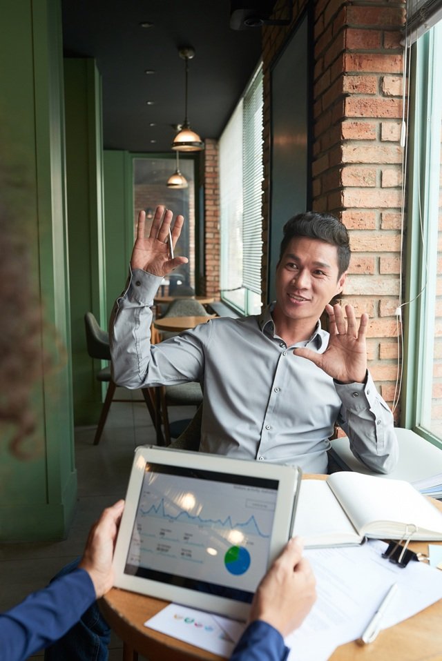 Cheerful Vietnamese businessman discussing start-up project with coworker in cafe